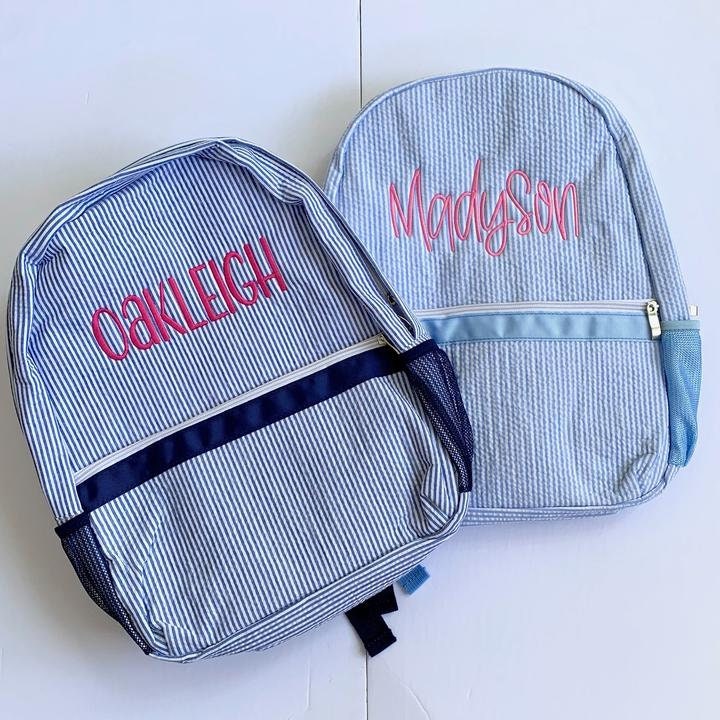 Navy seersucker backpack embroidered with Oakleigh in Hot Pink. Light Blue seersucker backpack with Madyson embroidered in light pink.